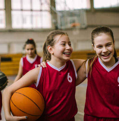 Jonge meisjes lachen en knuffelen elkaar na een basketbalmatch 